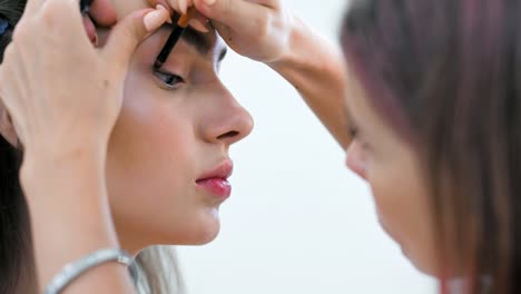 Close-up-hand-of-professional-make-up-artist-raising-upper-eyelid-of-model-for-painting-black-arrow