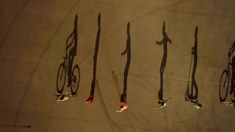 Children-riding-in-row-on-bikes,-roller-skates-and-scooters-cast-long-shadows.-Top-view