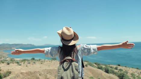 Medium-shot-active-female-traveler-in-sunglasses-and-hat-admiring-seascape-raising-hands