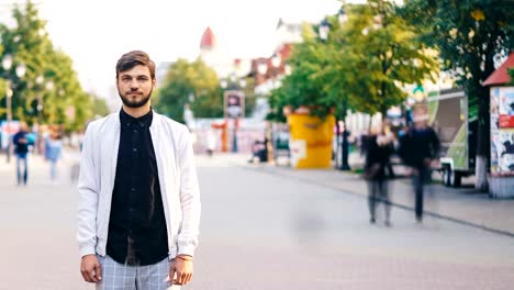 Time-lapse-of-handsome-guy-towny-standing-in-the-street-downtown-and-looking-at-camera-with-people-running-around.-Urban-lifestyle,-solitude-and-society-concept.