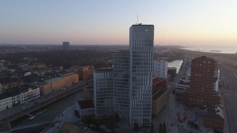 Aerial-view-of-modern-skyscraper-office-building-in-Malmö-city,-Sweden.-Drone-shot-flying-around-business-buildings-in-financial-district-at-sunset.-Cityscape-skyline-downtown,-canal-and-street