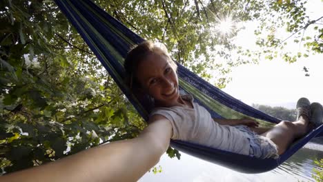 Joven-teniendo-selfie-en-hamaca-relajante-por-el-río-en-verano.-Tiempo-SELFIE