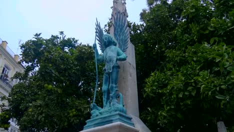 Bronze-statue-of-a-warrior-angel-against-a-fruit-tree-in-Valencia,-Spain