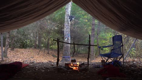 Wasserkocher-und-Topfaufhänger-mit-Lagerfeuer-und-Lichterketten.-Survival-Bushcraft-Setup-in-den-Blue-Ridge-Mountains-in-der-Nähe-von-Asheville.-Primitive-Tarp-Shelter