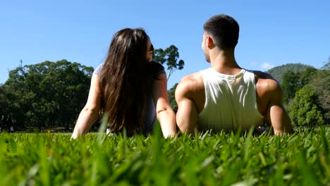 Young-couple-lying-on-green-grass-in-park-and-relaxing.-Man-and-woman-sitting-on-meadow-at-nature-and-kissing.-Girl-and-boy-looking-at-the-landscape-and-enjoying-vacation.-Rear-Back-Low-angle-of-view