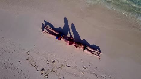 v03889-Aerial-flying-drone-view-of-Maldives-white-sandy-beach-2-people-young-couple-man-woman-romantic-love-on-sunny-tropical-paradise-island-with-aqua-blue-sky-sea-water-ocean-4k