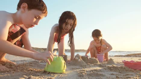 Drei-Kinder-spielen-am-Strand-Sandburgen-zusammen