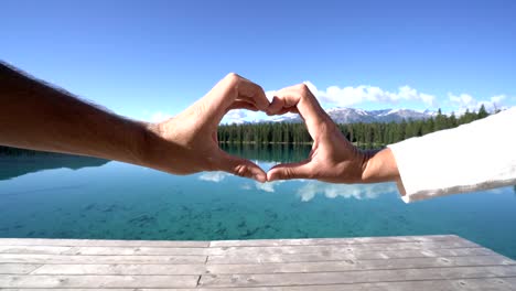 Cerrado-para-arriba-en-las-manos-de-la-pareja-hacer-un-marco-de-forma-de-corazón-en-el-lago