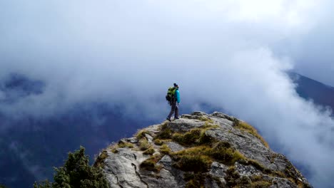 Girl-with-backpack-reaching-up-top-of-mountain-and-raised-hands