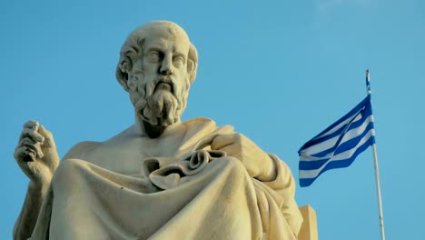 Primer-plano-de-una-estatua-de-mármol-del-gran-erudito-griego-de-la-antigüedad-de-Platón-en-el-fondo-de-la-bandera-nacional-de-Grecia.