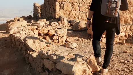 Man-with-backpack-steps-on-ancient-walls-ruins.-Caucasian-male-tourist-hikes-on-big-yellow-rocks.-Israel-Masada-4K