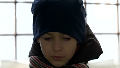 portrait-of-unhappy-boy-stands-alone-near-a-broken-window,-looking-into-the-camera,-cold-weather