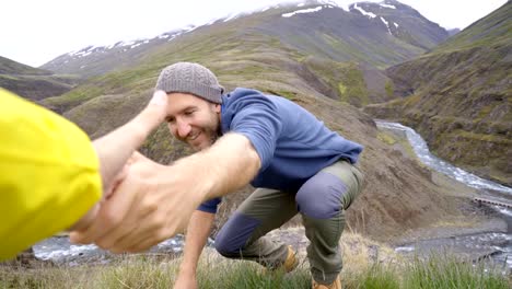 Excursionista-ayuda-a-su-compañero-de-equipo-para-llegar-a-la-cima-de-la-montaña-sobre-el-cañón-en-Islandia