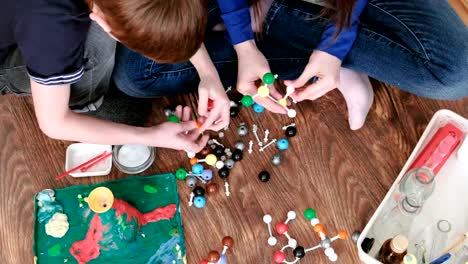 Closeup-hands-of-mom-and-son-building-molecule-models-of-colored-plastic-construction-set.-Top-view.