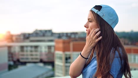 Side-view-portrait-of-young-attractive-teenage-woman-in-cap-enjoying-beautiful-sunset-outdoor