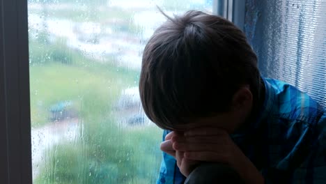 Crying-boy-looks-out-the-window-in-the-rain-and-is-sad.
