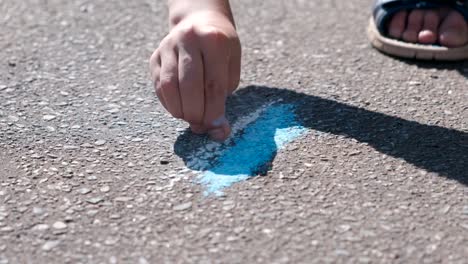 Junge-zieht-mit-blauer-Kreide-auf-dem-Asphalt.-Close-up-Hände.