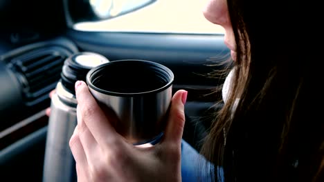 Vista-de-cerca-de-irreconocible-mujer-bebiendo-un-té-caliente-en-una-taza-termo-sentado-en-el-coche-en-invierno.