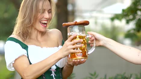 Mädchen-in-Bayerischer-Tracht-nimmt-ein-Glas-Bier-von-dem-Barkeeper-auf-dem-Bierfest-Oktoberfest.-Die-Frau-ist-glücklich-und-lacht,-ist-sie-überrascht-und-fröhlich.-Unter-freiem-Himmel