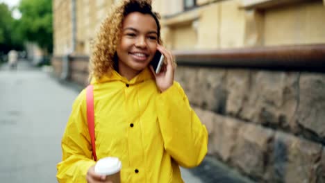 Schönes-Afroamerikanisches-Mädchen-ist-telefonieren-mit-Handy-und-halten-nehmen-Weg-Kaffee-im-Stadt-Straße-entlang-spazieren-und-genießen-Gespräch-lachen.