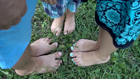 Bare-feet-on-green-grass.-Dad,-mom-and-a-small-child-stand-with-their-bare-feet-next-to-each-other-on-the-lawn-in-the-Park.-Close-up-legs.-The-view-from-the-top.