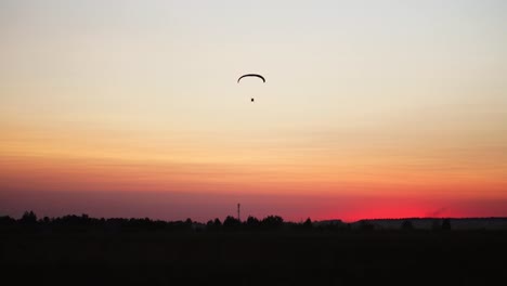 El-piloto-de-un-parapente-vuela-desde-la-cámara-poco-a-poco-alejándose-en-la-distancia-contra-el-hermoso-cielo-al-atardecer.-Imagen-de-fondo-de-fondo-hermoso.-concepto-de-libertad