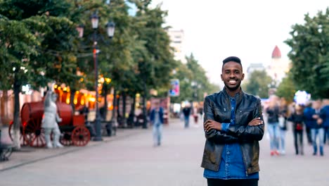 Time-lapse-del-sonriente-hombre-afroamericano-solas-en-el-centro-con-las-manos-cruzadas-disfrutando-de-la-vida-de-la-ciudad-y-mirando-a-cámara.-Concepto-de-estilo-de-vida-y-juventud.