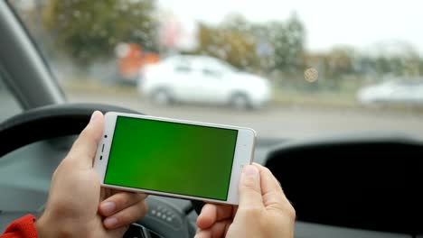 Mano-sosteniendo-el-smartphone-con-la-pantalla-en-blanco-verde-en-coche-para-masaje,-ubicación,-dirección,-negocios.-Vida-de-la-ciudad.-Hombre-se-sienta-en-el-coche-y-funciona-en-smartphone-pantalla-verde-closeup.-Clave-de-croma.-Día-de-lluvia.