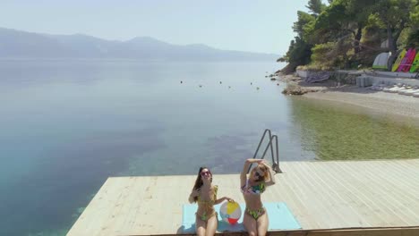 Aerial-view-of-two-women-sits-on-wooden-deck-in-Panagopoula,-Greece.