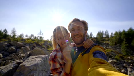 Hikers,-couple--taking-selfie-portrait-on-mountain-trail.-sun-shining-over-the-mountains.-Beautiful-sunbeam-effect-making-an-idyllic-landscape.-Young-couple-hiking-take-video-selfie-in-Switzerland