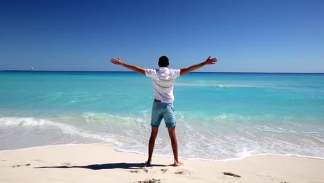 Young-man-standing-on--beach-with-outstretched-hands