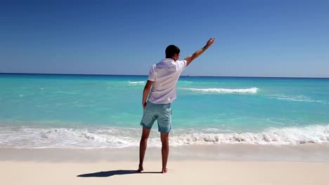 Young-man-standing-on-beach-and-showing-at-the-sky