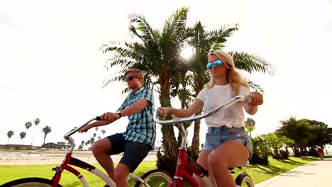 Pareja-joven-montando-bicicletas-en-la-playa-en-cámara-lenta