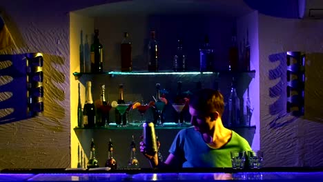 Barman-joven-haciendo-trucos-con-dos-copas,-un-agitador-y-botella-standing-behind-the-bar,-ver,-tirando-en-cámara-lenta