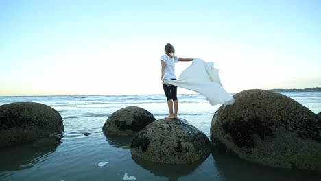 One-female-stands-on-boulder,-holds-blanket-in-the-air