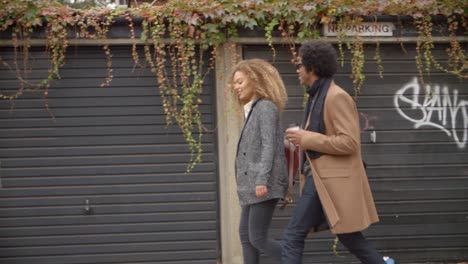 Stylish-Young-Couple-Walking-Past-Garages-On-City-Street