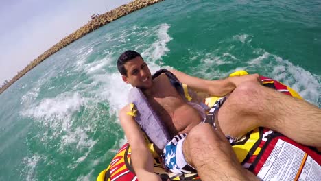 Man-sitting-in-inflatable-ring-towed-by-a-boat-in-the-water-and-recording-himself-with-Go-Pro-camera