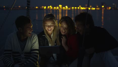 Gruppe-von-Personen-mit-Tablet-auf-einem-Segelboot-im-Meer-in-der-Nacht.