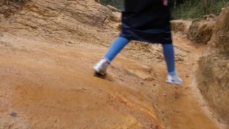 Nach-der-weibliche-Touristen-in-Regenmantel-zu-Fuß-auf-Stone-Mountain-Trail.-Die-Füße-der-Frau-durch-eine-schmale-Schlucht-wandern.-Die-Beine-des-Mädchens-in-Turnschuhen-auf-den-steinigen-Weg-gehen.-Geringe-Blickwinkel-hautnah