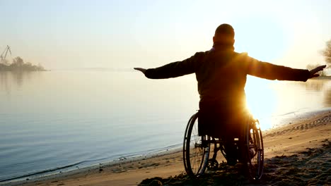 cripple-person-hands-up,-sundown-on-wheel-chair,-lonely-disabled-on