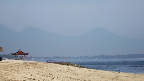 Wellen-des-warmen-Meeres-laufen-am-Sandstrand-des-tropischen-Resorts-mit-Sonnenschirmen-und-Liegestühlen