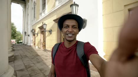 Happy-mixed-race-tourist-man-having-online-video-chat-using-his-smartphone-camera-standing-near-historical-building-in-Europe