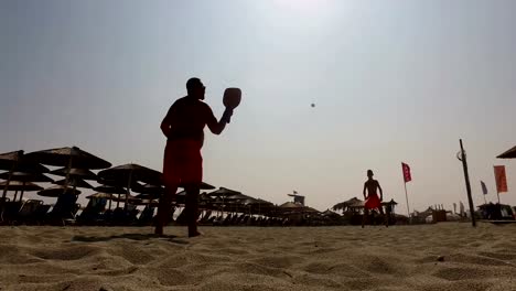 Silueta-de-dos-hombres-jugando-al-tenis-playa-en-la-playa