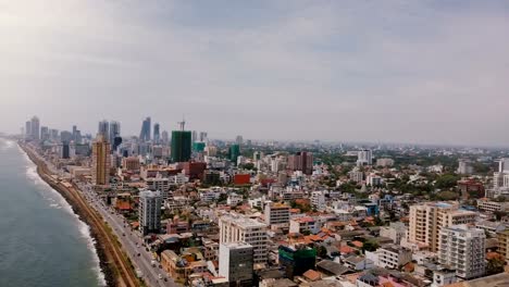 Drone-panning-right-over-beautiful-coastline,-modern-buildings-of-Colombo,-Sri-Lanka.-Aerial-view-of-Asian-cityscape