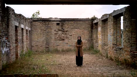 Young-muslim-woman-in-hijab-standing-alone-in-ruined-abandoned-brick-building