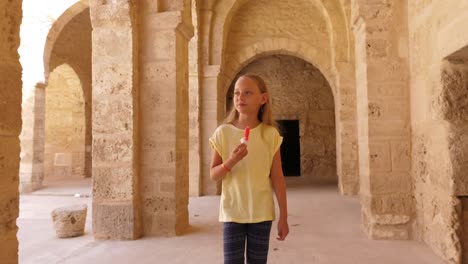 Young-girl-walking-and-eating-ice-cream-on-background-with-arch-from-beige-stones