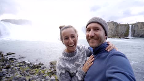 Viaje-pareja-diversión-tomando-fotos-selfie-por-cascada-Godafoss-en-Islandia-con-smartphone.-La-gente-visita-lugares-de-interés-turístico-y-monumentos-en-la-ruta-1