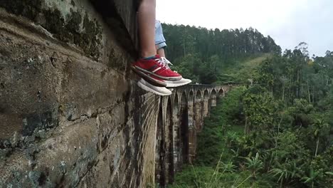 4K-TVEAD:-madre-e-hijo-ubicación-y-oscilación-de-pies-en-los-nueve-arcos-Demodara-puente-en-Ella,-Sri-Lanka:-cerrar-pies-de-imagen