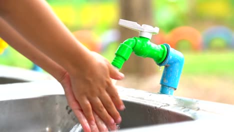 Water-tap-open-pouring-water-to-cleaning-hand-of-child.-Clean-water-flowing-out-from-vale-pipe-to-sink.-Close-up-hand-and-faucet-water-tap