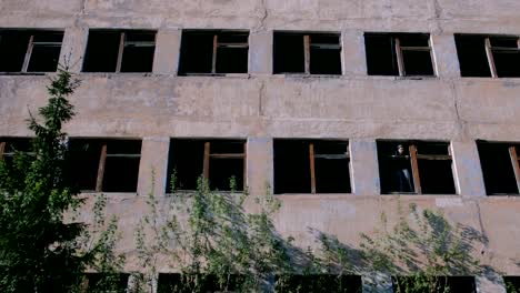 Woman-standing-on-window-of-destroyed-multi-storey-building-with-many-broken-windows.